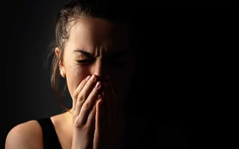 Visage d'une femme en larmes, mains sur la bouche, exprimant la détresse et les symptômes du stress post-narcissique.