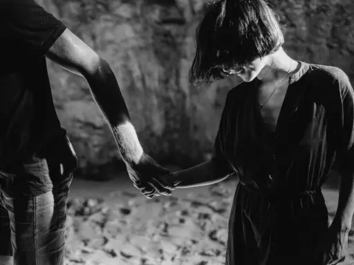 Un couple se tient la main dans un décor rocheux. L'homme, un hpi manipulateur, guide la femme dans l'ombre.