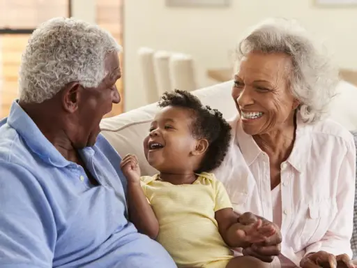 Un bébé rit aux éclats, entouré de ses grands-parents. La grand-mère, loin d'être indifférente, partage la joie de son petit-enfant.