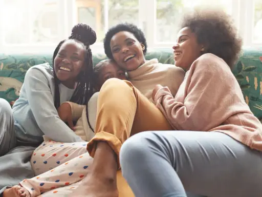 Une famille rit aux éclats sur un canapé. L'ainé de la famille, la plus grande, est au centre, entourée de ses sœurs.