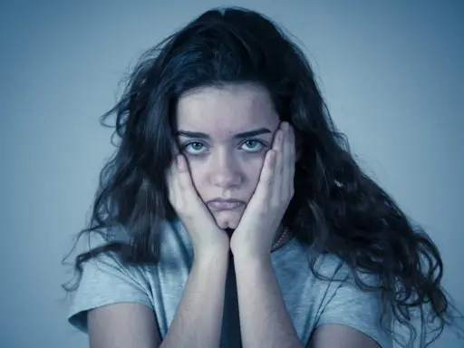 Jeune femme aux mains sur les joues, regard perdu. Elle semble passer un test de sociopathe, l'air accablé.