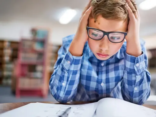 Garçon avec lunettes, mains sur la tête, visiblement en difficulté face à ses devoirs. Signes adolescent HPI, difficultés scolaires.
