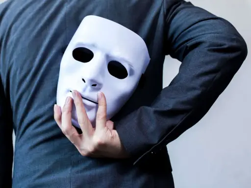 Une main cache un masque blanc derrière un costume. "Je suis narcissique, que faire ?" se demande la personne.