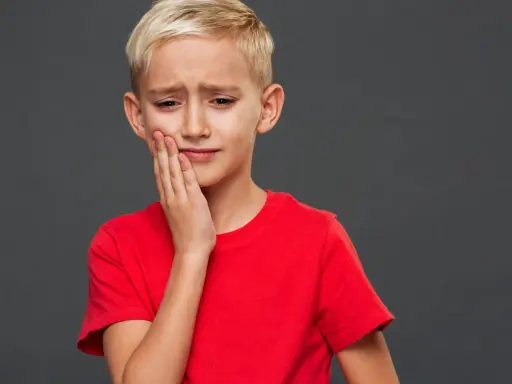 Un jeune garçon blond, le visage crispé, se tient la joue. Il semble triste, comme si mon fils se sent mal aimé.