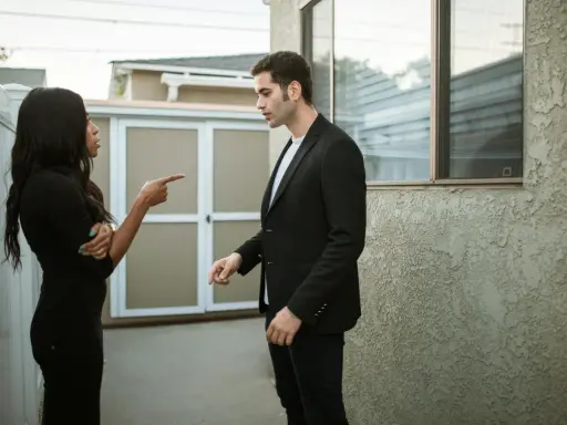 Une femme noire en robe noire pointe du doigt un homme en costume noir, lui reprochant quelque chose. Elle semble vouloir lui faire regretter quelqu'un.