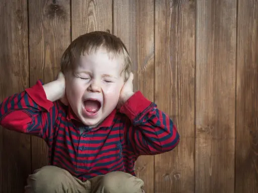 Petit garçon de 5 ans, yeux fermés, criant fort, mains sur les oreilles, en pleine crise de colère incontrôlable.