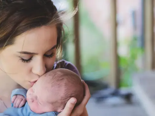 Une jeune femme, peut-être enceinte à 18 ans, embrasse tendrement son bébé.