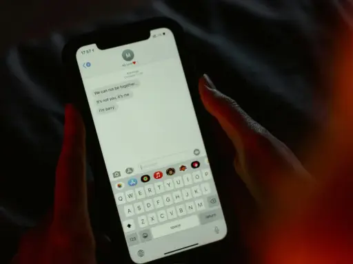 Main tenant une main sur un smartphone, affichant une conversation de rupture. Une tentative maladroite de faire rire son ex par sms.