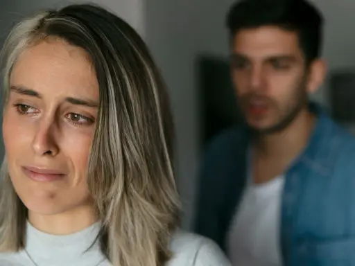 Une femme au regard triste, un homme flou en arrière-plan. Pourquoi un homme cache qu'il a une copine ? Une situation compliquée.