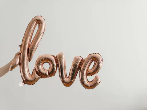 Ballon rose doré formant le mot "love", tenu par une main. Un coup de foudre sans connaître la personne, une promesse d'amour.