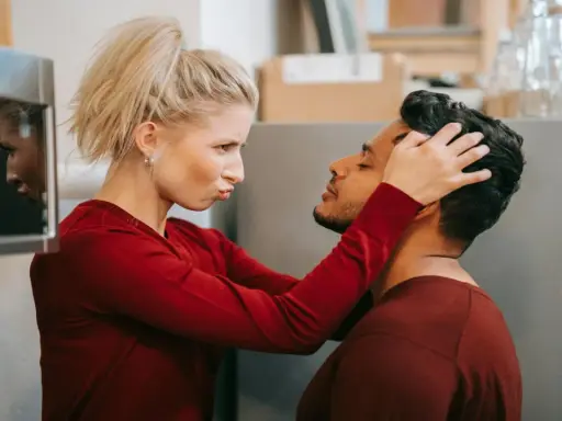 Une femme possessive ajuste la tête de son partenaire, le regardant avec une expression intense.