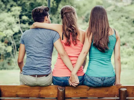 Trois personnes assises sur un banc, deux femmes se tenant la main dans le dos, un homme au milieu. Une scène qui interroge sur comment faire avouer à un homme qu'il vous trompe.