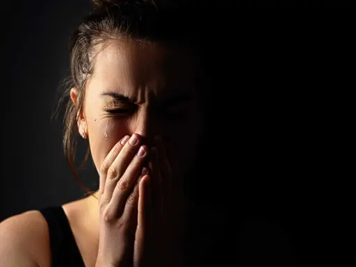 Visage d'une femme en larmes, mains sur la bouche, exprimant la détresse et les symptômes du stress post-narcissique.