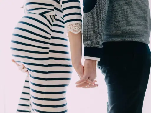 Une femme enceinte et son mari se tiennent la main. Elle porte une robe rayée, lui un pull. Il semble qu'il ne la soutienne pas pendant sa grossesse.