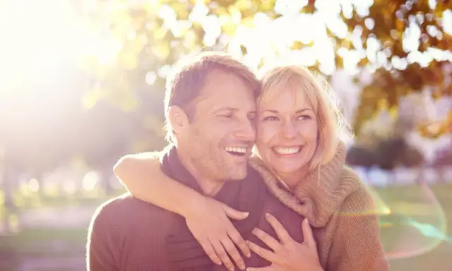 Un couple souriant, peut-être traversant une crise de la cinquantaine, mais l'infidélité semble loin. Lumière dorée d'automne.
