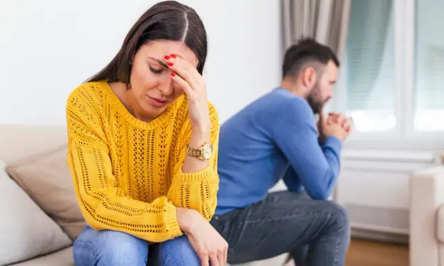 Une femme désemparée se tient la tête, son mari pensif est assis dos à elle. Elle se demande comment savoir si mon mari me trompe.