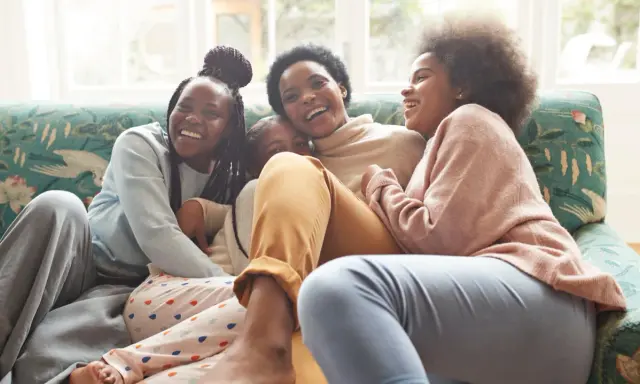 Une famille rit aux éclats sur un canapé. L'ainé de la famille, la plus grande, est au centre, entourée de ses sœurs.