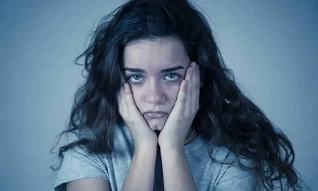 Jeune femme aux mains sur les joues, regard perdu. Elle semble passer un test de sociopathe, l'air accablé.