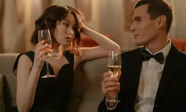 Un homme en smoking et une femme en robe noire sirotent du champagne, une scène qui pourrait inspirer sur comment séduire une fille.