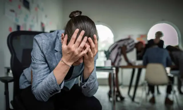 Personse tenant la tête entre les mains, visiblement stressée. Un test d'anxiété sociale pourrait révéler son état.
