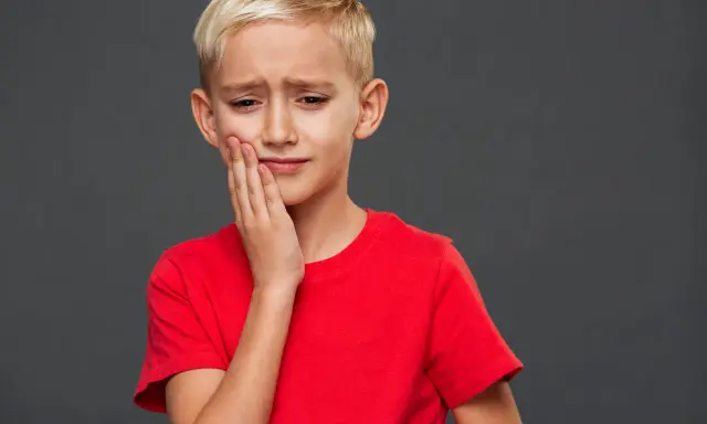 Un jeune garçon blond, le visage crispé, se tient la joue. Il semble triste, comme si mon fils se sent mal aimé.