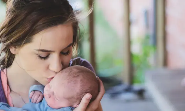 Une jeune femme, peut-être enceinte à 18 ans, embrasse tendrement son bébé.