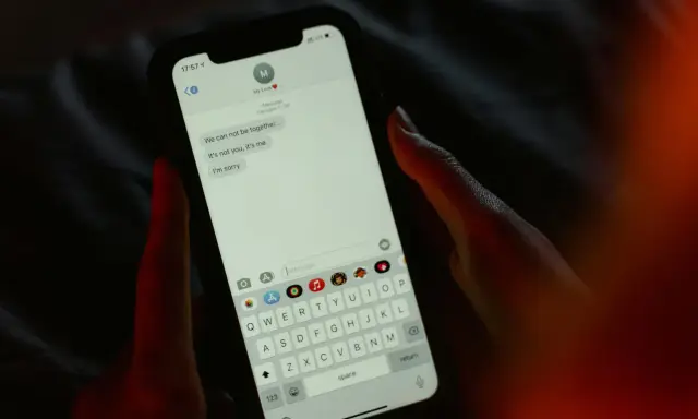 Main tenant une main sur un smartphone, affichant une conversation de rupture. Une tentative maladroite de faire rire son ex par sms.