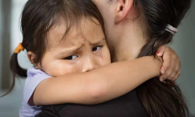 Un enfant serre sa mère, le regard plein d'angoisse de séparation.