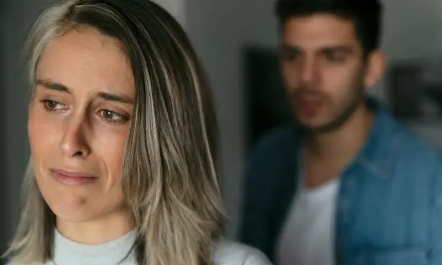 Une femme au regard triste, un homme flou en arrière-plan. Pourquoi un homme cache qu'il a une copine ? Une situation compliquée.