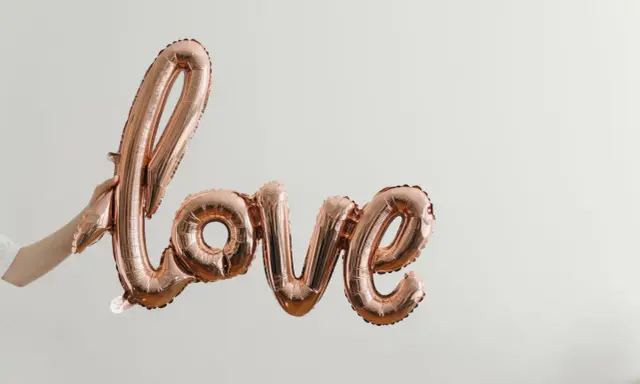Ballon rose doré formant le mot "love", tenu par une main. Un coup de foudre sans connaître la personne, une promesse d'amour.