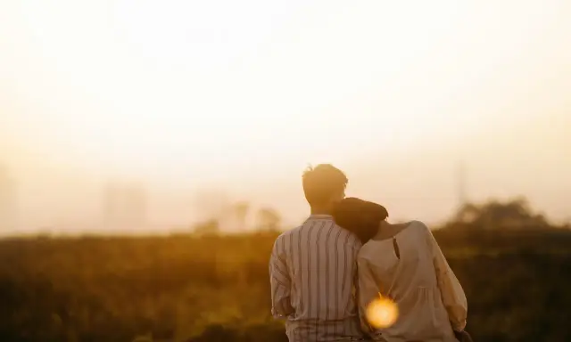 Couple assis dos à dos, la tête de la femme posée sur l'épaule de l'homme, au coucher du soleil.