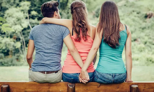Trois personnes assises sur un banc, deux femmes se tenant la main dans le dos, un homme au milieu. Une scène qui interroge sur comment faire avouer à un homme qu'il vous trompe.