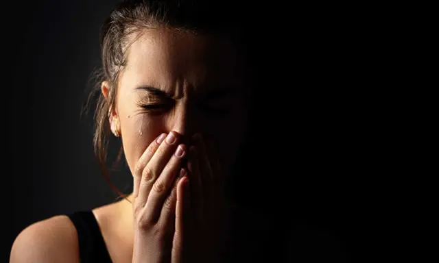 Visage d'une femme en larmes, mains sur la bouche, exprimant la détresse et les symptômes du stress post-narcissique.