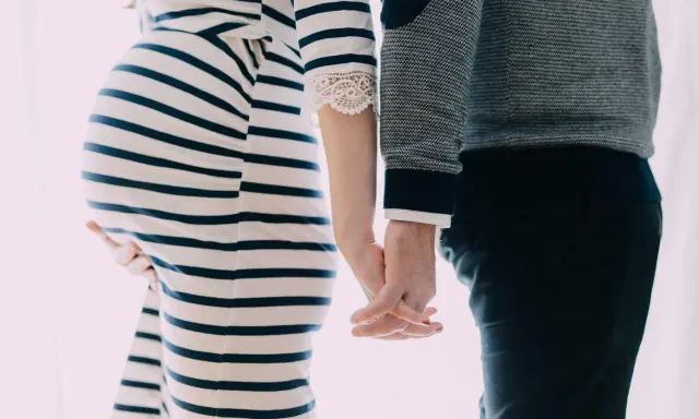 Une femme enceinte et son mari se tiennent la main. Elle porte une robe rayée, lui un pull. Il semble qu'il ne la soutienne pas pendant sa grossesse.
