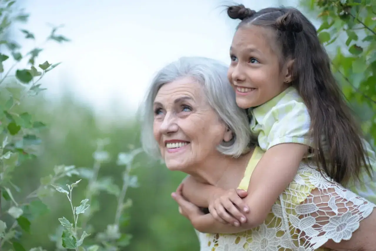 Une petite fille fait un gros c&acirc;lin &agrave; sa grand-m&egrave;re indiff&eacute;rente, toutes deux regardant vers le ciel avec des sourires radieux.