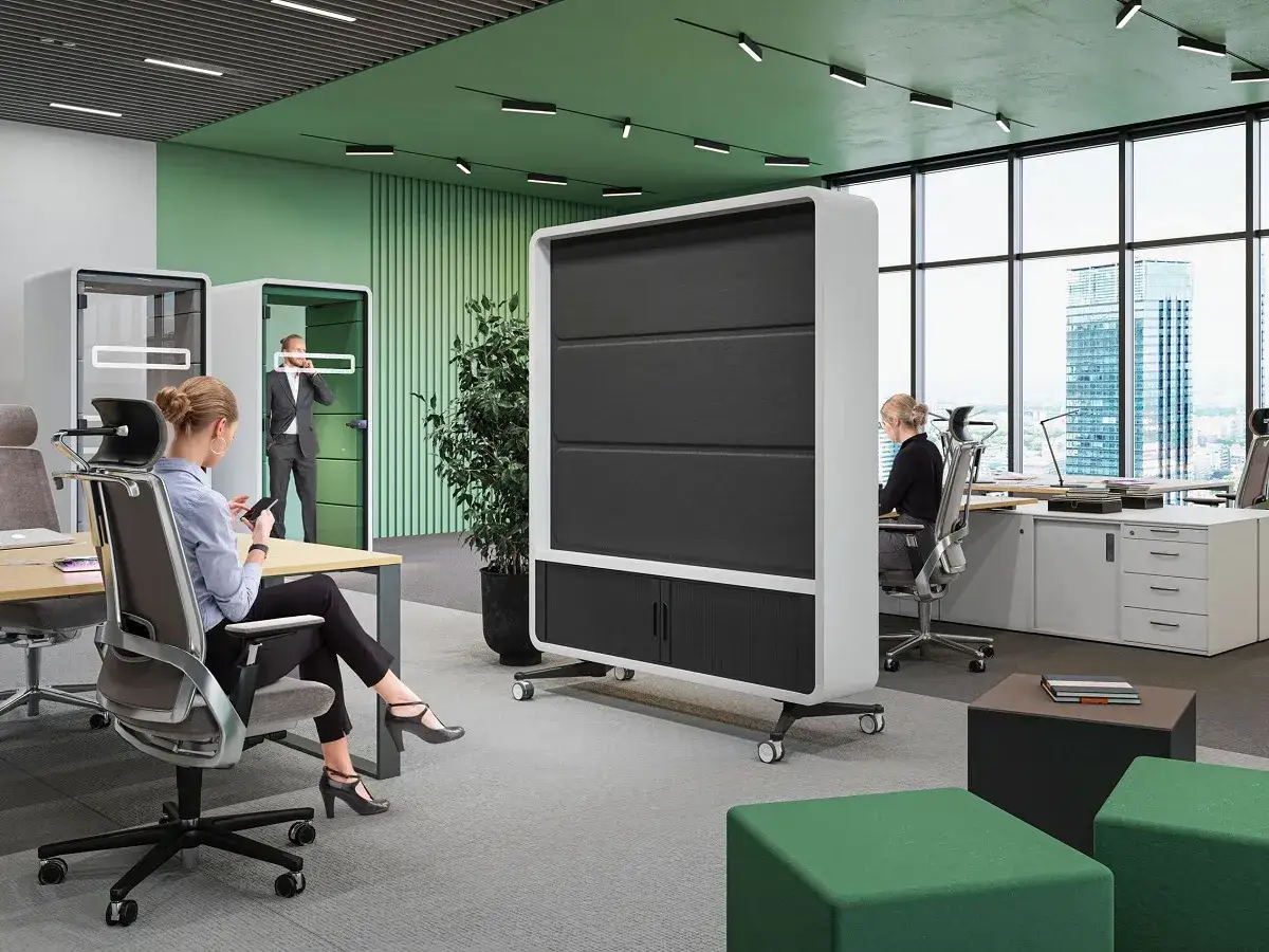 Dans un bureau moderne, une femme regarde son t&eacute;l&eacute;phone, assise &agrave; son bureau. Un homme en costume parle au t&eacute;l&eacute;phone dans une cabine insonoris&eacute;e. Une sc&egrave;ne qui pourrait rappeler le d&eacute;fi de travailler avec son ex.