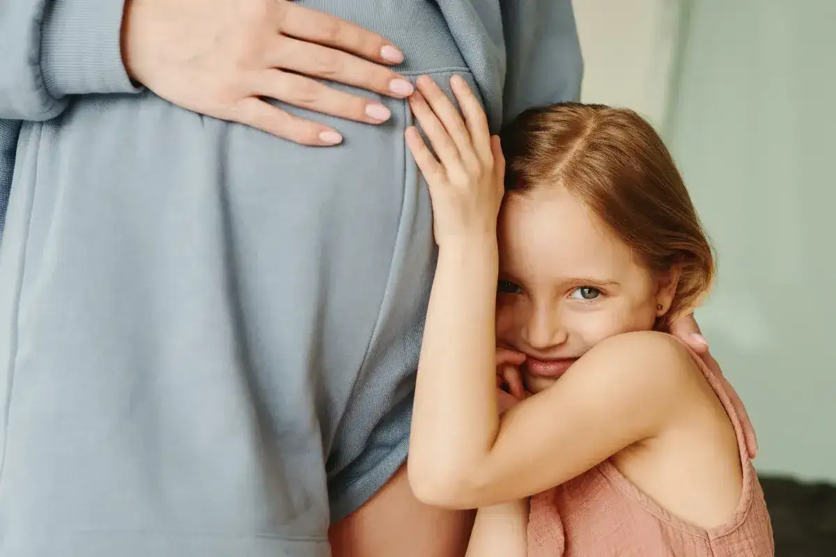 Une petite fille aux cheveux roux enlace tendrement le ventre arrondi de sa m&egrave;re, l'a&icirc;n&eacute;e ressent la grossesse avec une joie palpable.