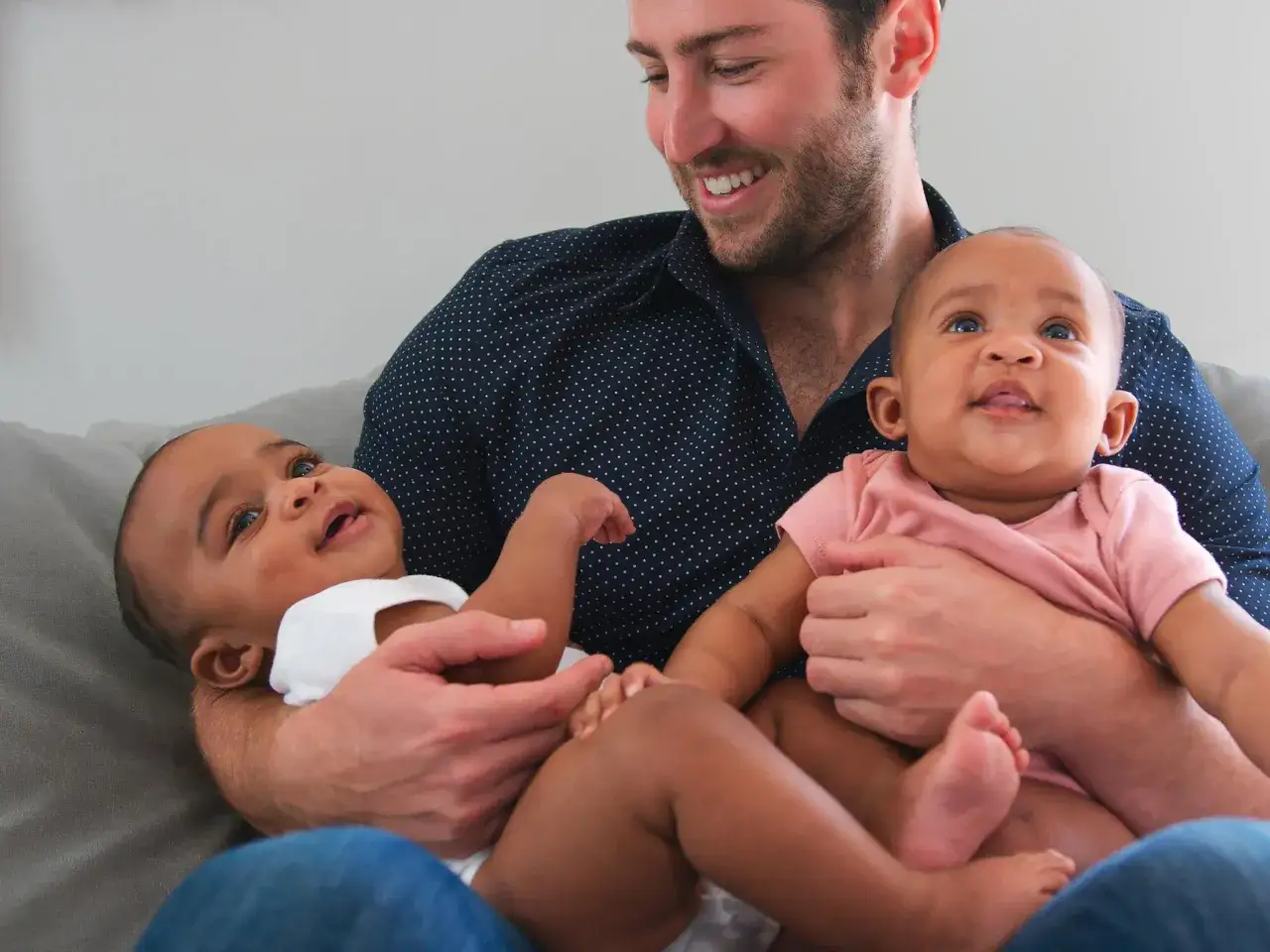 Un homme souriant tient deux bébés, une maman de jumeaux comblée.