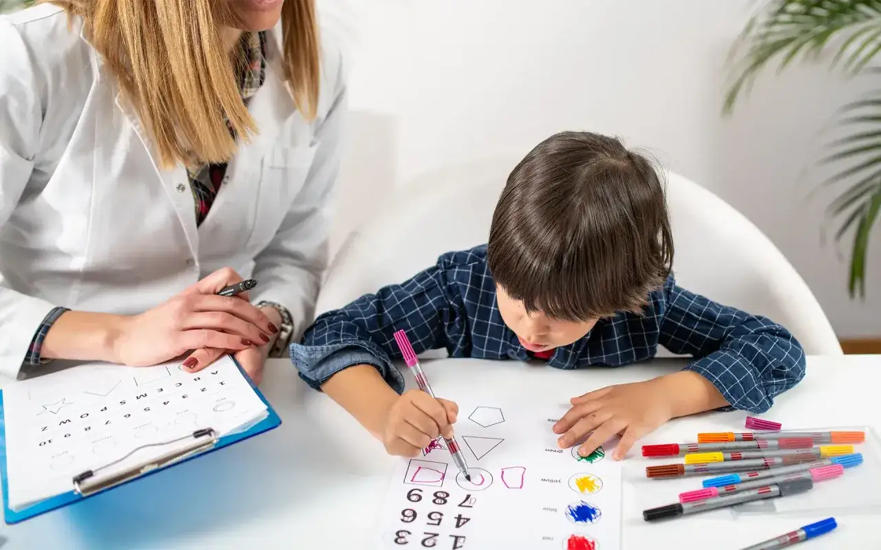 Un enfant concentr&eacute; dessine des formes lors d'un test pour &eacute;valuer sa dyslexie. Une orthophoniste observe attentivement.