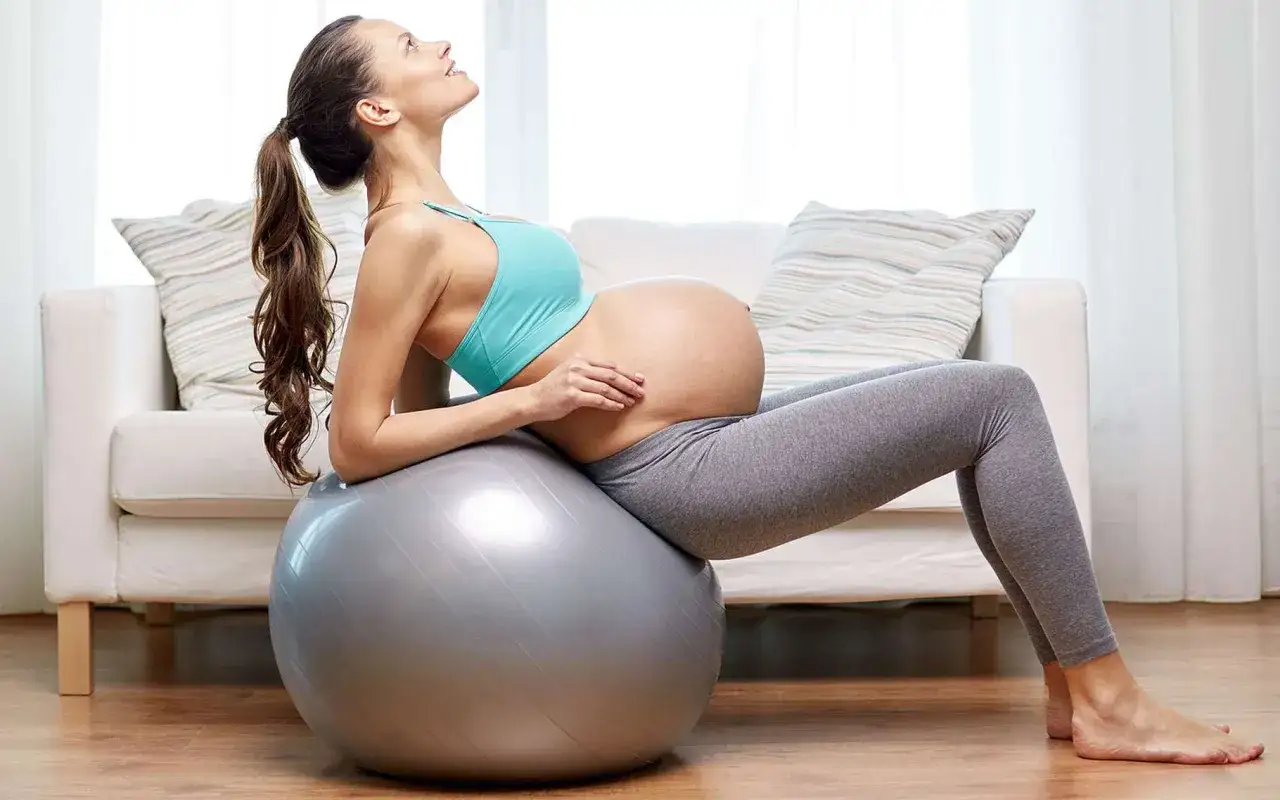 Femme enceinte souriante sur un ballon de gym, un message encouragement avant accouchement.