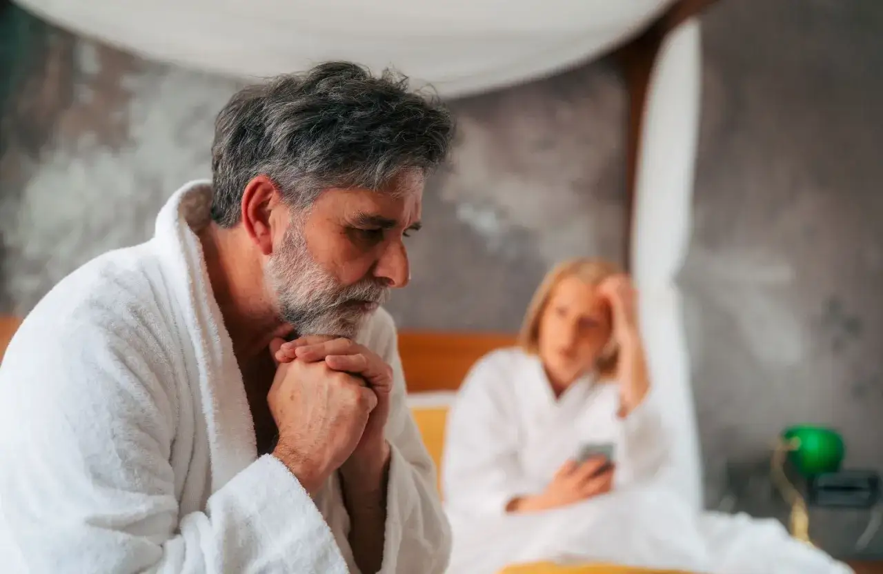 Un homme d'&acirc;ge m&ucirc;r, pensif, en robe de chambre blanche, semble traverser une crise de la cinquantaine, peut-&ecirc;tre li&eacute;e &agrave; une infid&eacute;lit&eacute;. Sa femme, floue &agrave; l'arri&egrave;re-plan, consulte son t&eacute;l&eacute;phone.