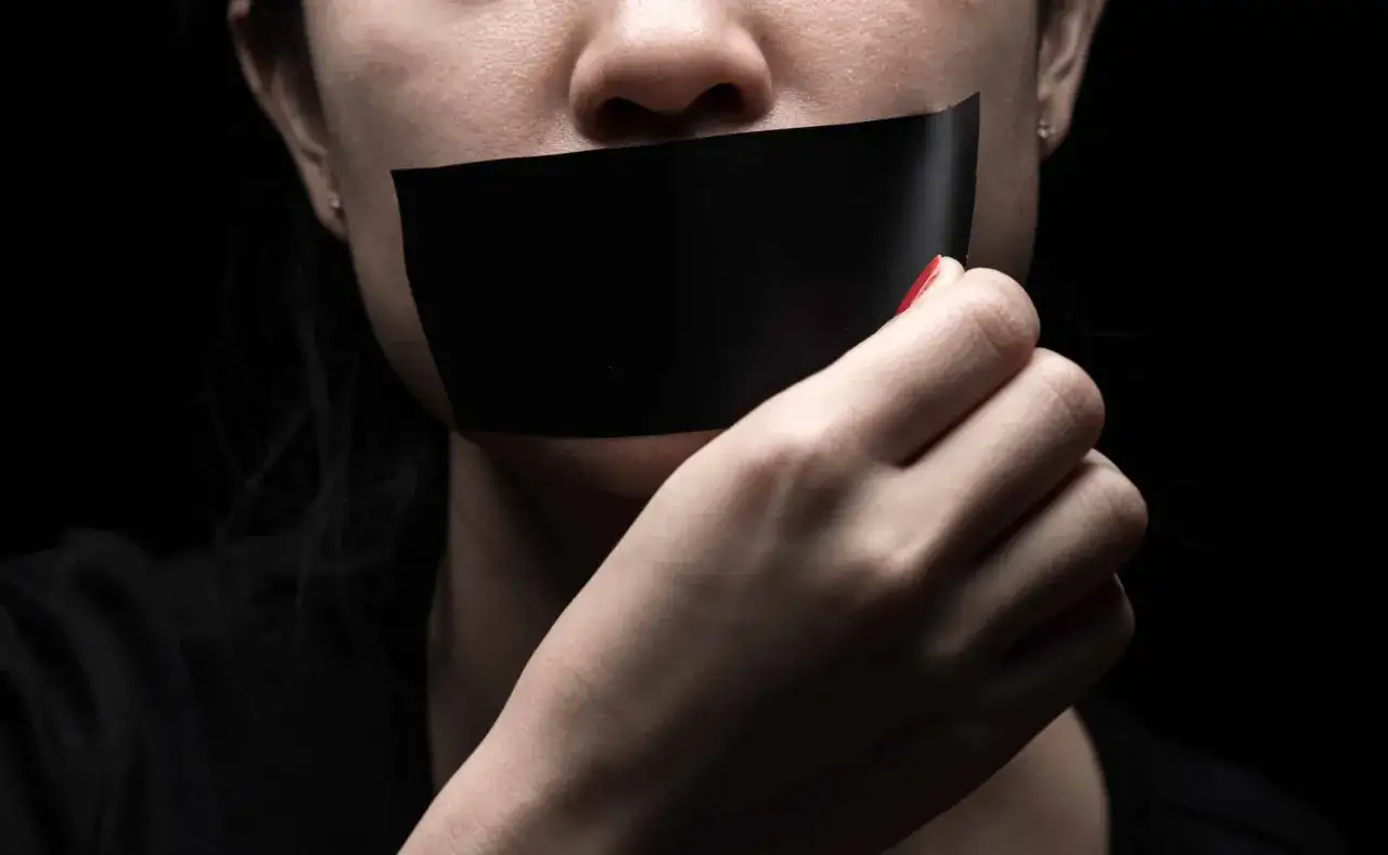 Une bouche b&acirc;illonn&eacute;e par du ruban adh&eacute;sif noir, une main tentant de le retirer. L'effet du silence sur le manipulateur est palpable.