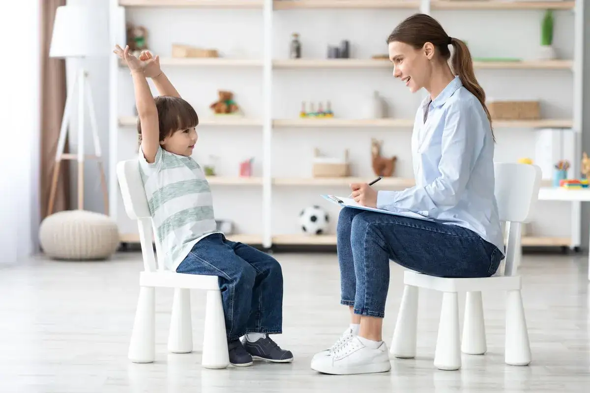 Un enfant hpi neuroatypique, mains en l'air, interagit avec une thérapeute qui prend des notes.