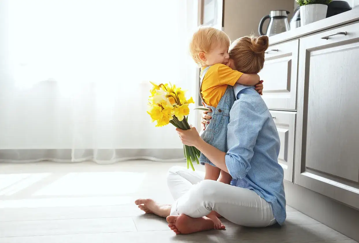 Un enfant enlace sa m&egrave;re, lui offrant un bouquet de jonquilles. Une sc&egrave;ne touchante qui illustre l'amour inconditionnel d'une m&egrave;re.
