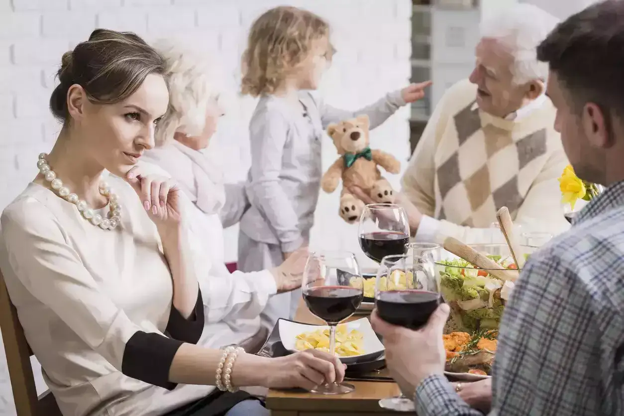 Une femme se sent exclue de sa belle-famille lors d'un repas, son regard pensif contrastant avec la joie des autres autour de la table.