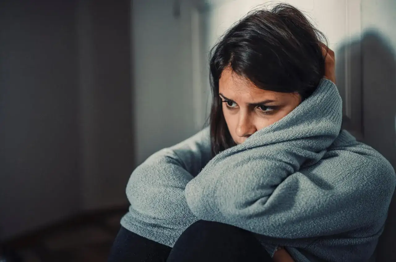 Femme seule, le regard perdu, recroquevill&eacute;e dans un pull gris. Elle semble revivre les tourments d'une relation malsaine avec son ex.