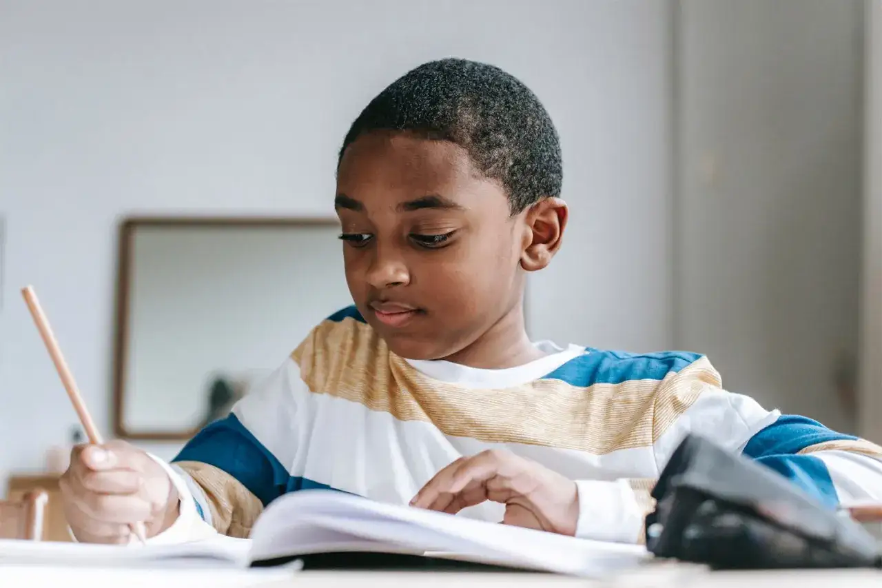 Un jeune garçon concentré sur son cahier, crayon à la main. Il révise sérieusement, peut-être pour un test pour sauter une classe.