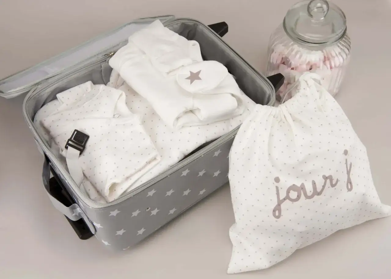 Valise grise &eacute;toil&eacute;e pr&ecirc;te pour un accouchement seule sans papa. V&ecirc;tements de b&eacute;b&eacute; blancs, sac 