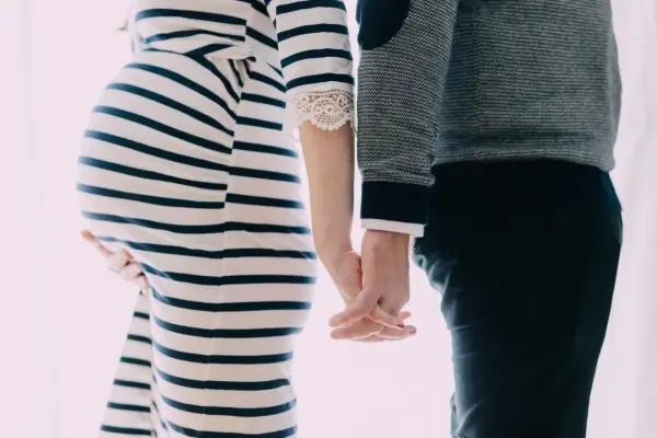 Une femme enceinte et son mari se tiennent la main. Elle porte une robe rayée, lui un pull. Il semble qu'il ne la soutienne pas pendant sa grossesse.