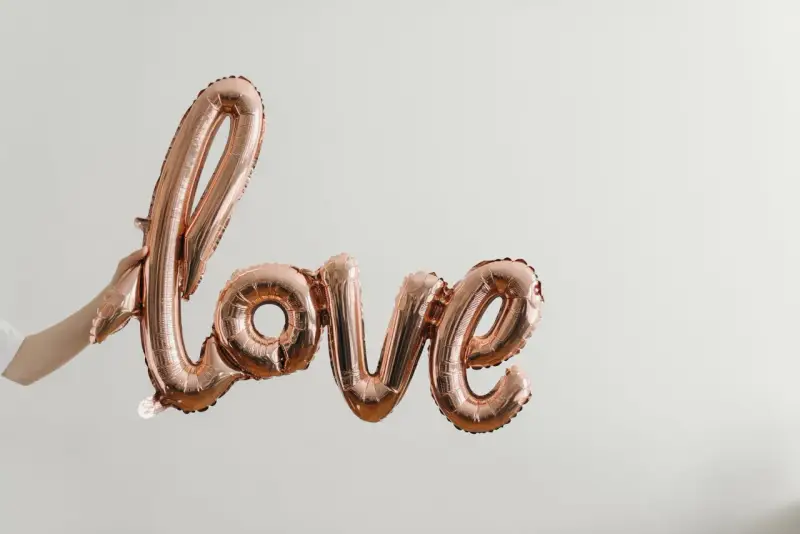 Ballon rose doré formant le mot "love", tenu par une main. Un coup de foudre sans connaître la personne, une promesse d'amour.